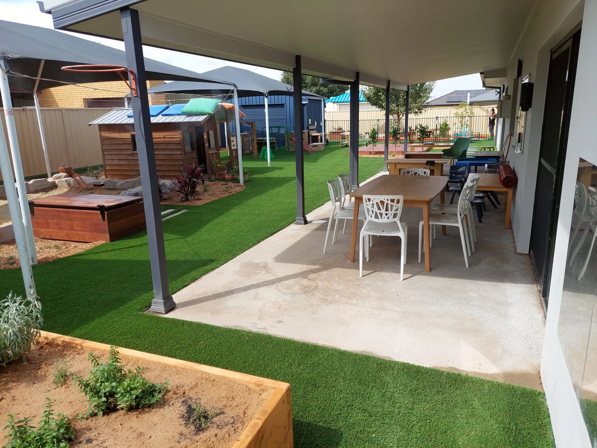 Childcare centre covered outdoor dining area beside synthetic turf and garden beds