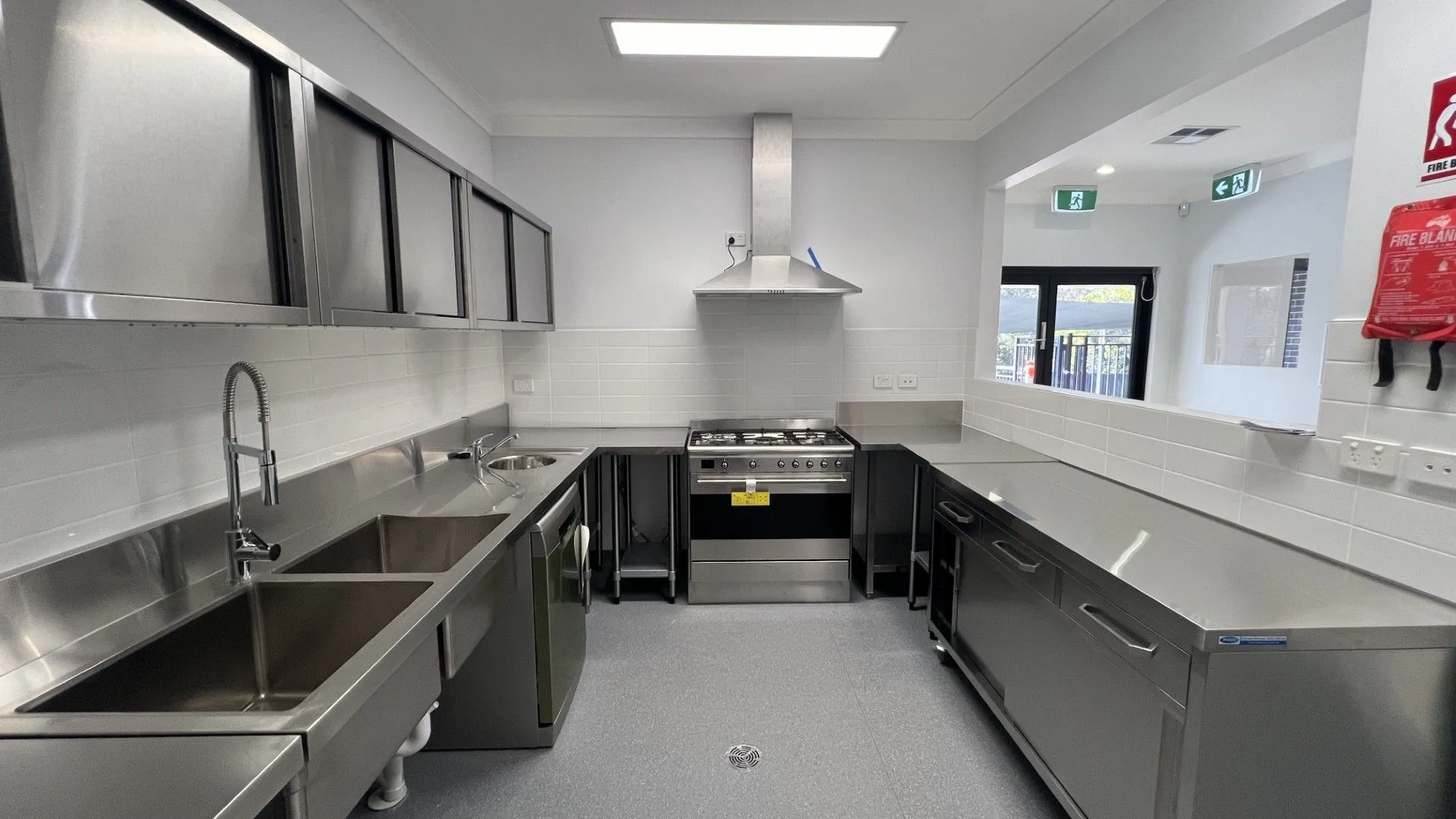 Childcare centre commercial kitchen with stainless benches, double sink and servery window