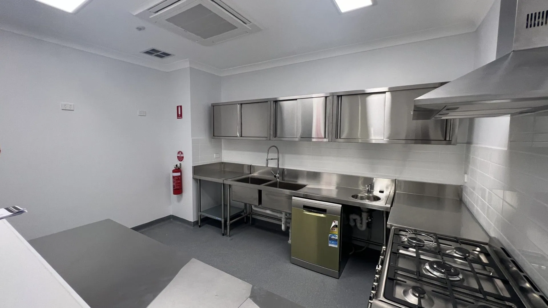 Stainless steel commercial kitchen with gas cooktop and rangehood in a childcare centre fitout