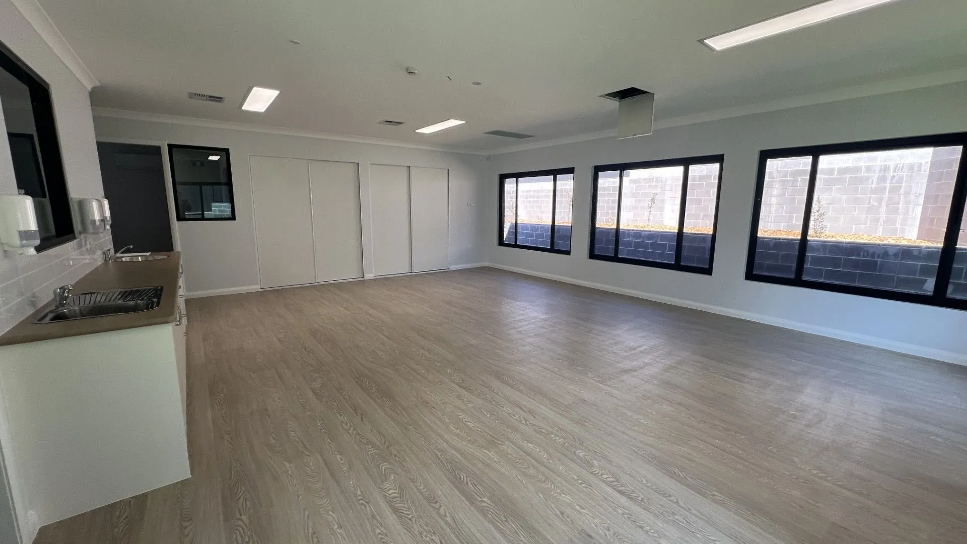 Open childcare playroom with kitchenette, high windows and timber look flooring