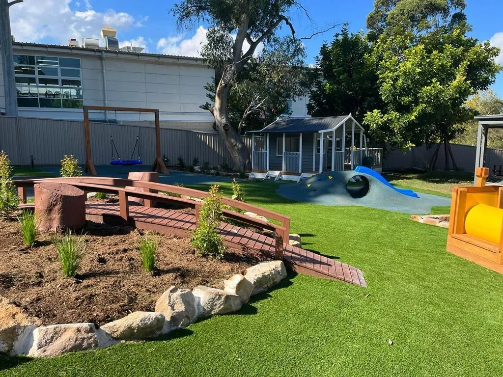 Childcare centre outdoor play area with synthetic turf, timber play equipment and sandstone garden edging