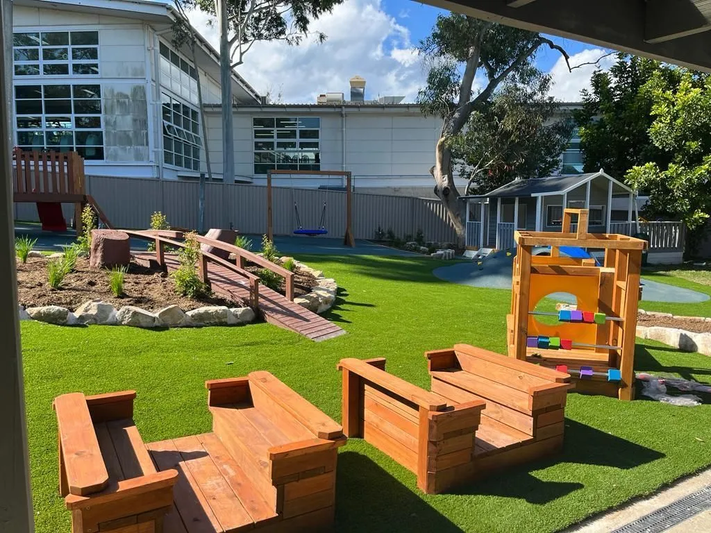 Childcare centre playground with synthetic turf, timber seating and sensory play panels