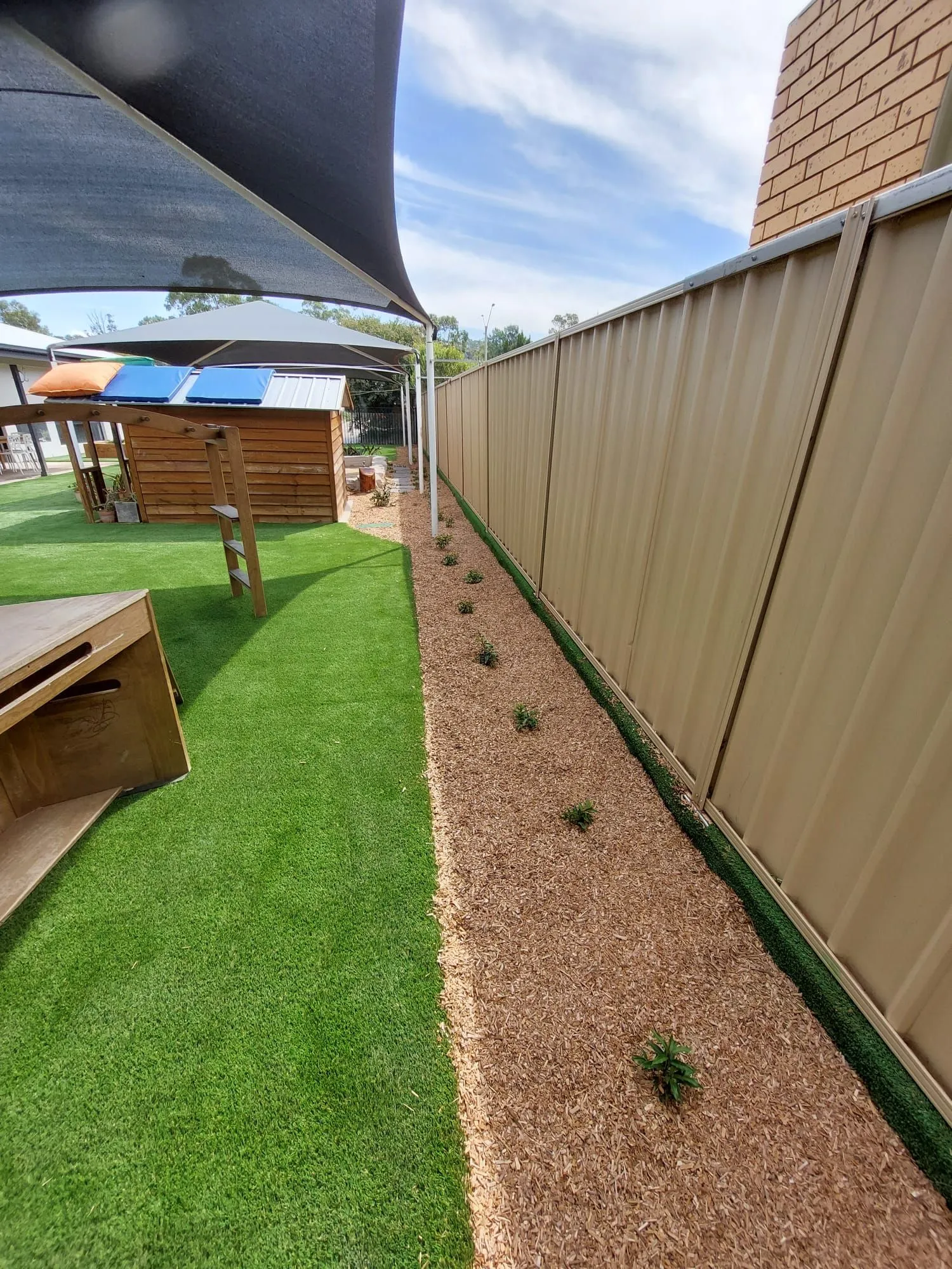 Side garden path with synthetic turf and new planting along a childcare centre fence
