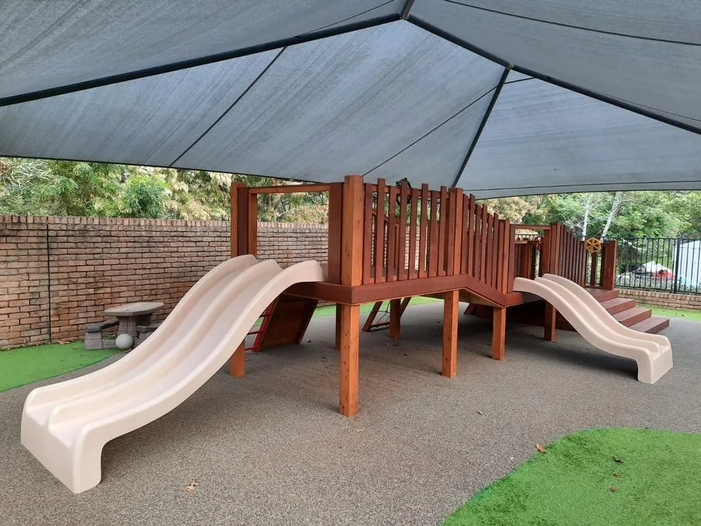 Childcare timber play fort with twin slides under a shade structure