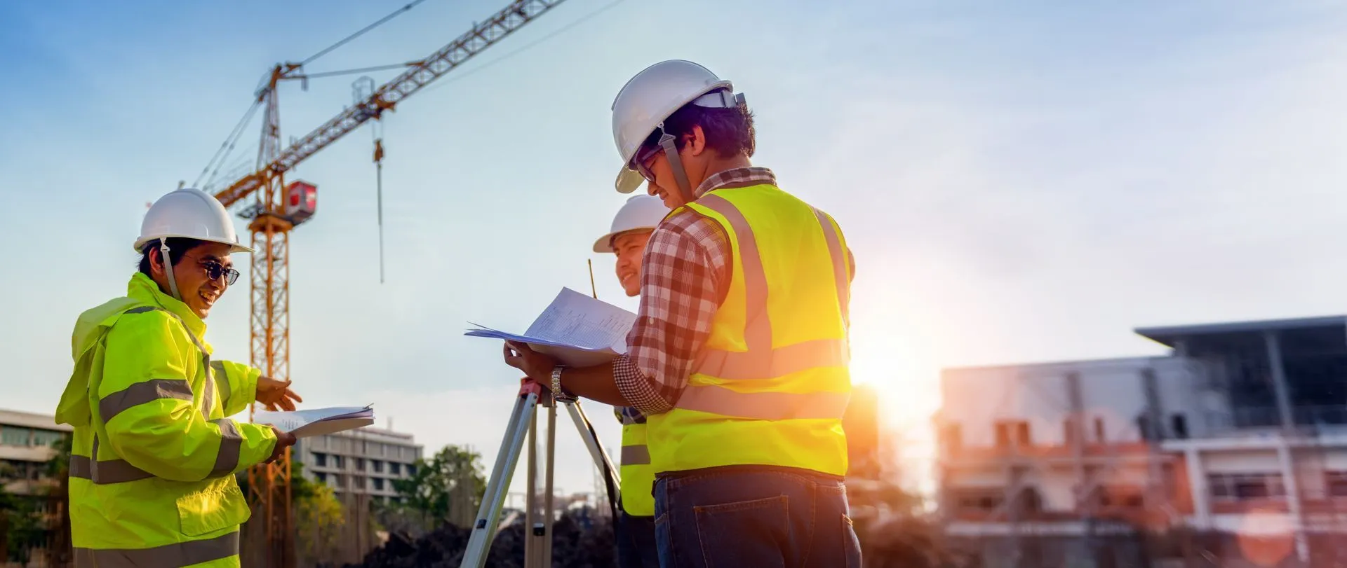 Engineers in hard hats reviewing plans on a construction site with a tower crane
