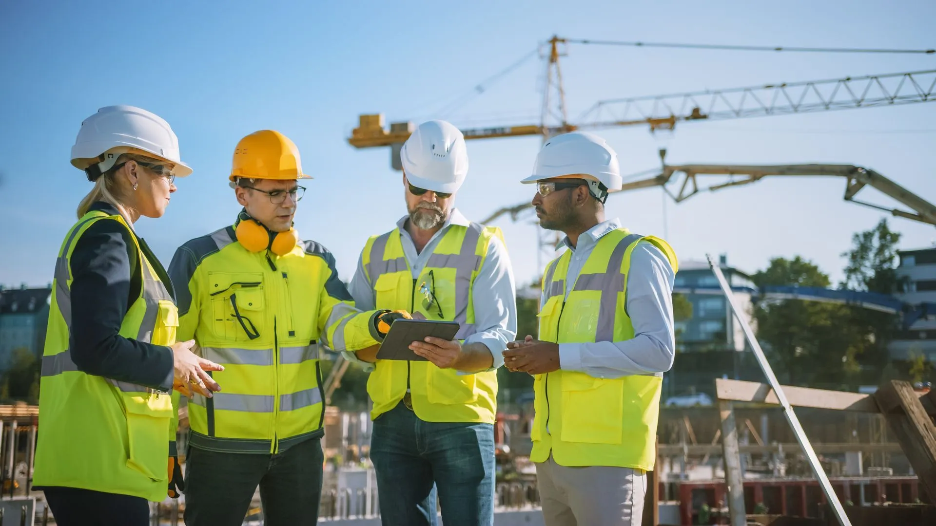 Project managers in hard hats and high visibility vests reviewing a tablet on a construction site