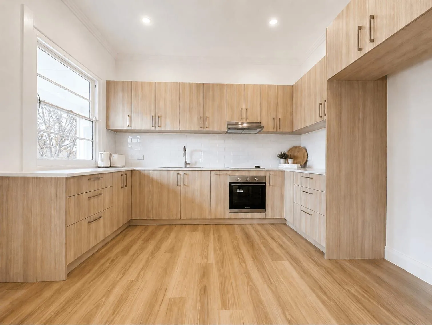 Renovated kitchen with timber look cabinetry, white splashback and timber flooring, Wyong whole home renovation